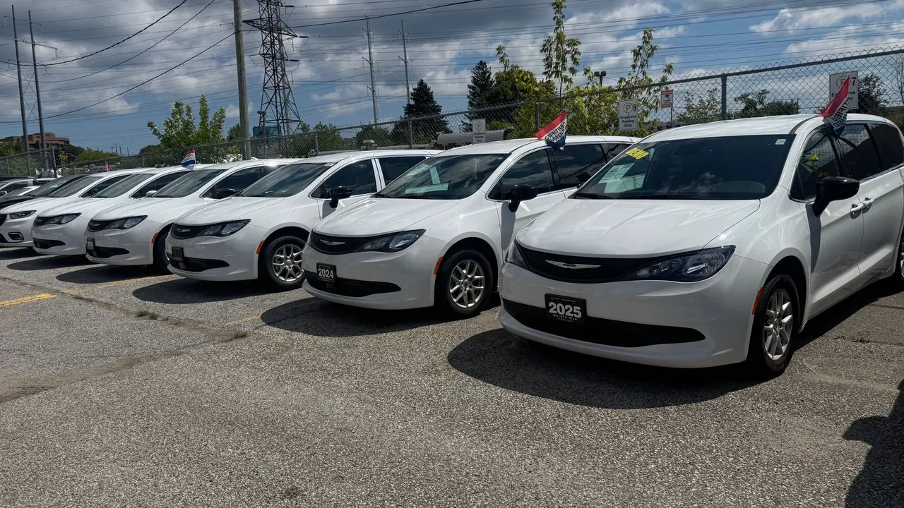 A row of white Chrysler Grand Caravan minivans parked on the lot at Golden Mile Chrysler, Toronto