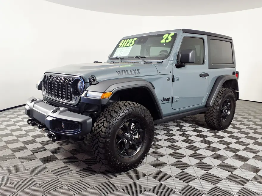 2025 Jeep Wrangler Willys (JL) in Anvil grey, front three-quarter view showing the Willys hood decal, gloss-black grille and 33-inch mud-terrain tires